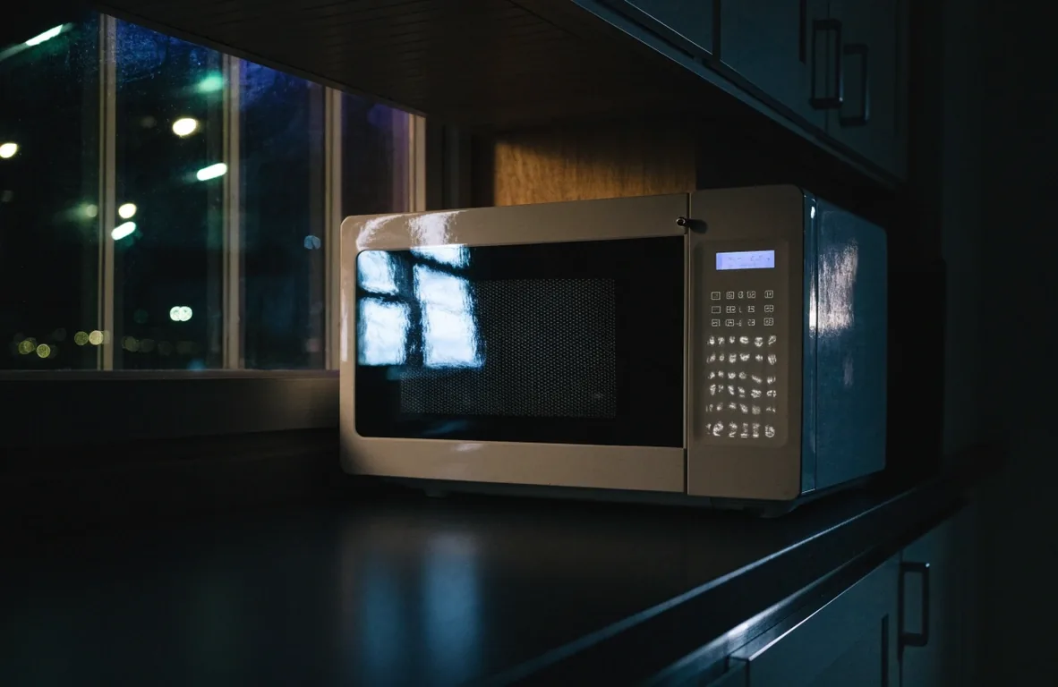 Microondas digital en una cocina de noche con reflejo frío en la puerta